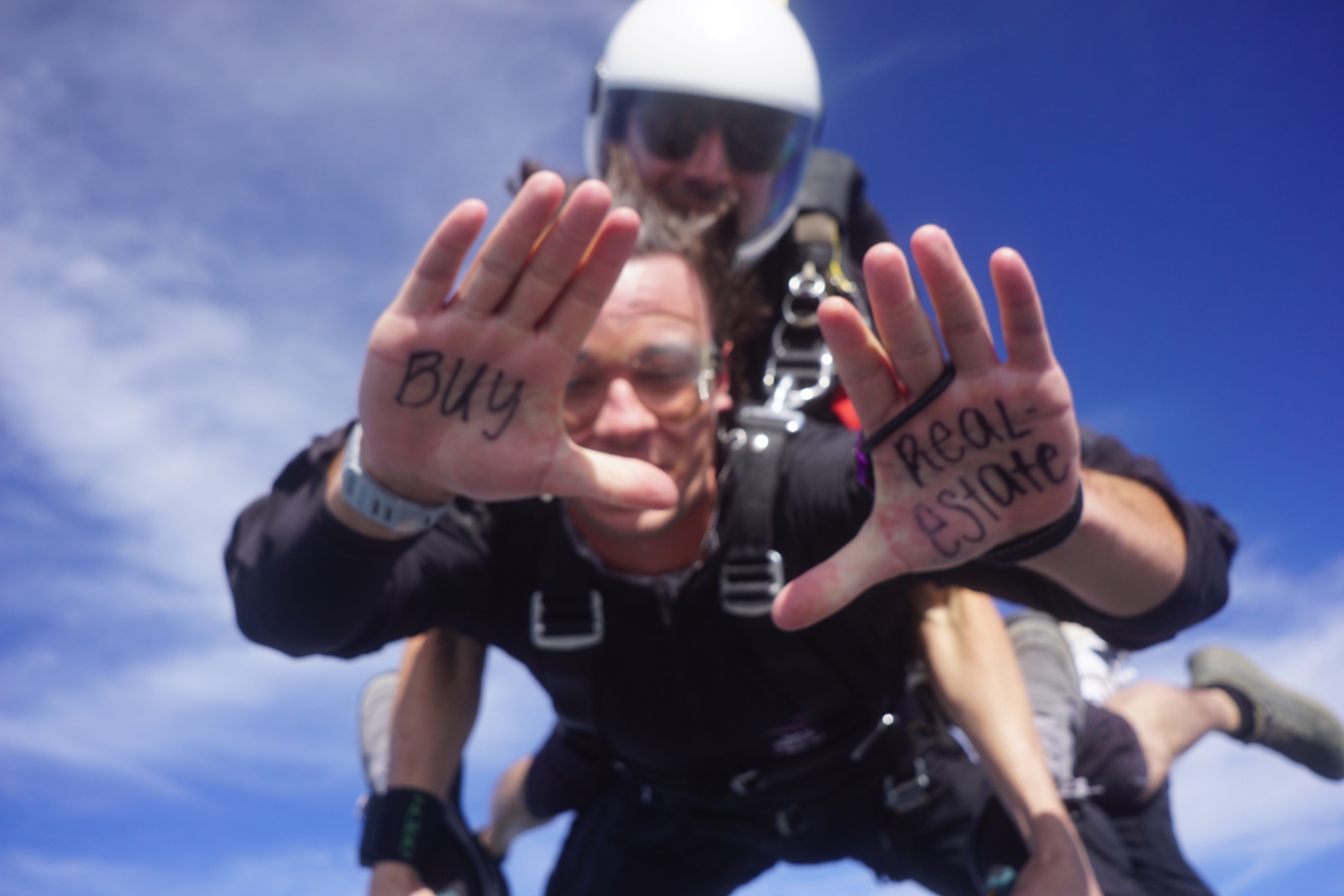Zac Hamilton skydiving with Buy Real Estate written across his hands